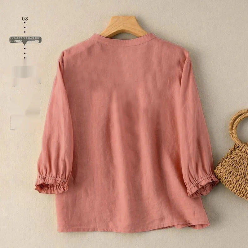 Back view of a pink long-sleeve blouse with gathered cuffs hanging on wooden hanger against beige wall
