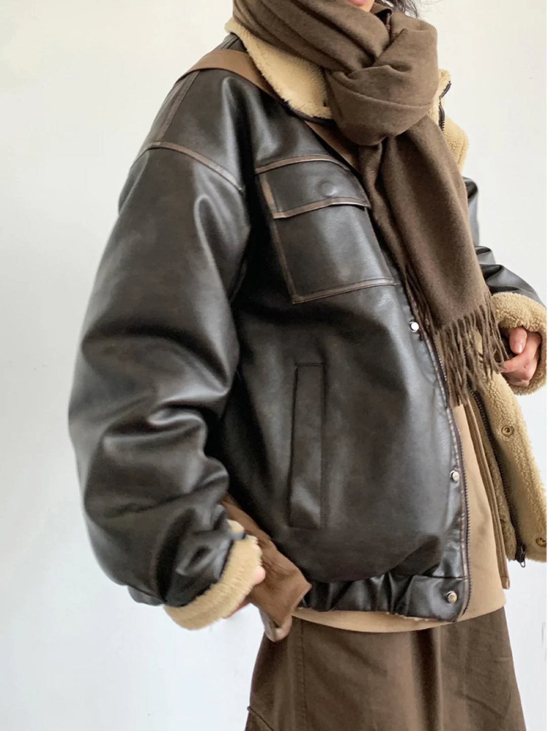 Person wearing dark brown leather shearling jacket and brown wool scarf against white background