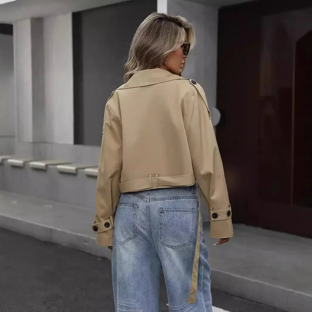 Woman wearing beige cropped trench coat and light blue jeans standing on urban sidewalk