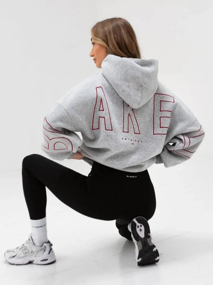 Woman wearing grey oversized hoodie with red letters and black leggings in white studio