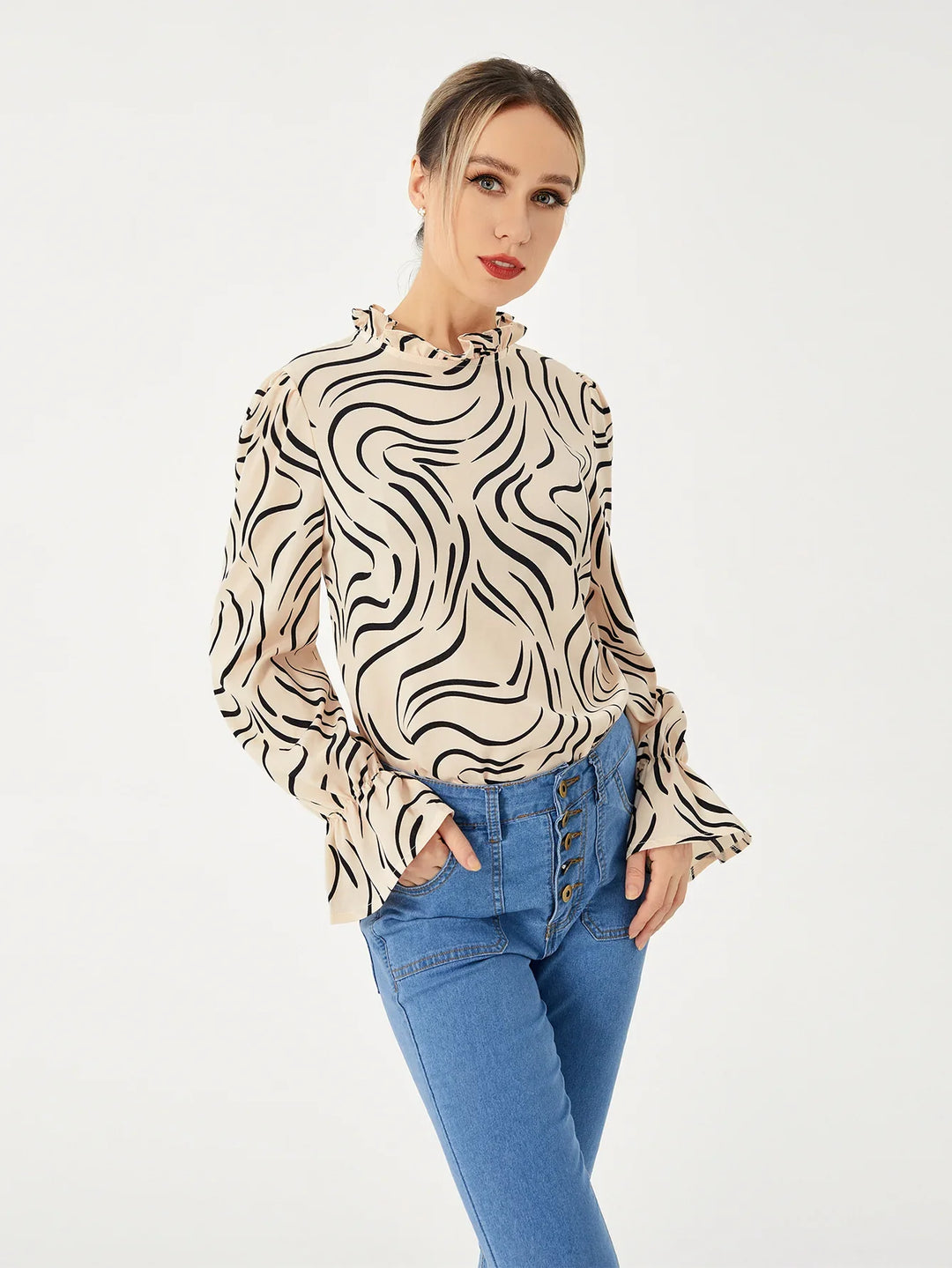 Woman wearing a beige long sleeve blouse with black swirl patterns and high-waisted blue jeans