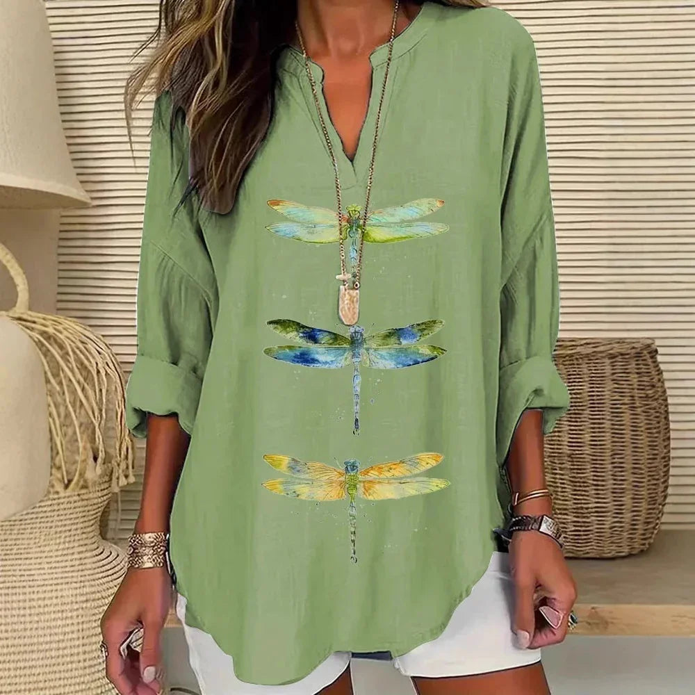 Woman wearing a green V-neck blouse with colorful dragonfly prints, paired with white shorts