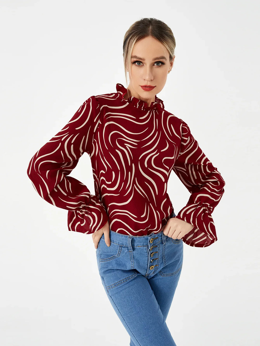 Woman wearing a red and white abstract print blouse with ruffled collar and high-waisted buttoned blue jeans
