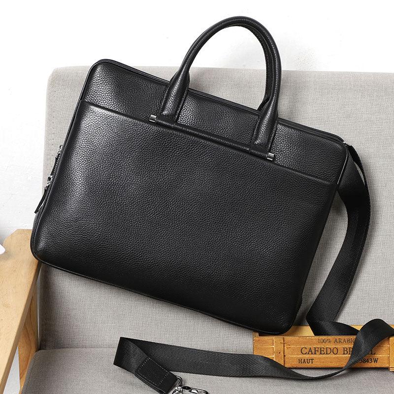 Black textured leather briefcase with handles and detachable shoulder strap on beige chair