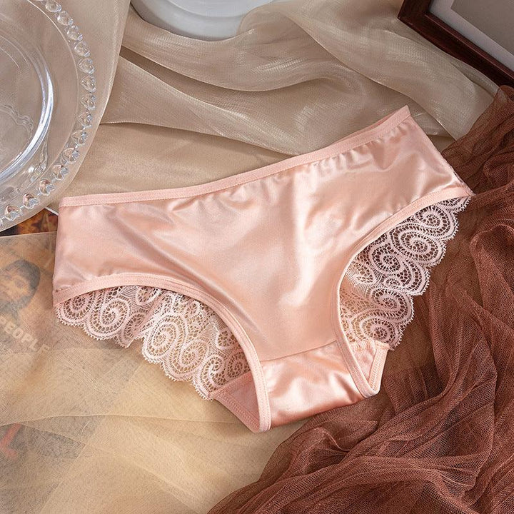 Soft pink satin women's panties with intricate lace trim on a beige and brown fabric background