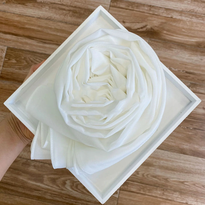 Hand holding a white box with a rolled white fabric resembling a rose on wooden floor background