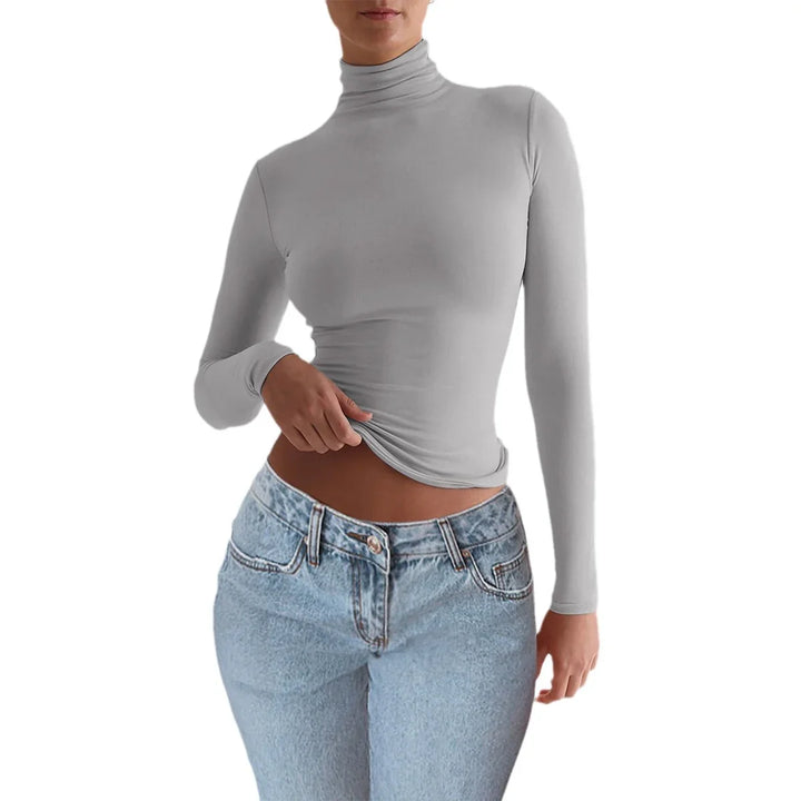 Woman wearing fitted light gray turtleneck long sleeve top and high-waisted blue jeans