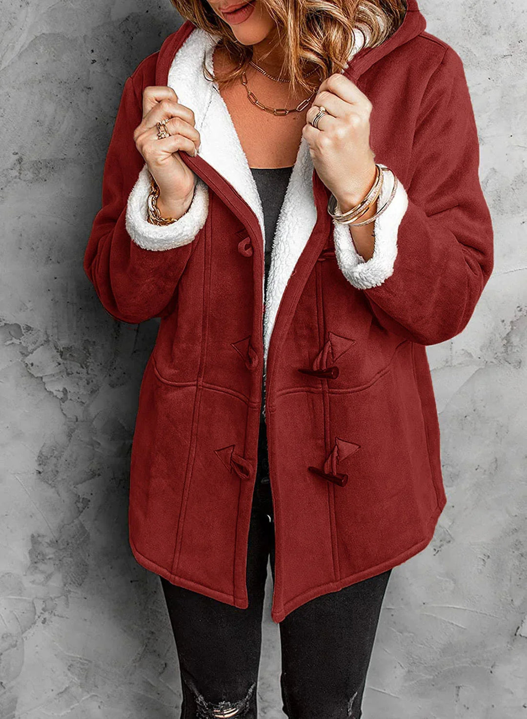 Woman wearing rust red toggle coat with white sherpa lining and hood, styled with layered gold jewelry
