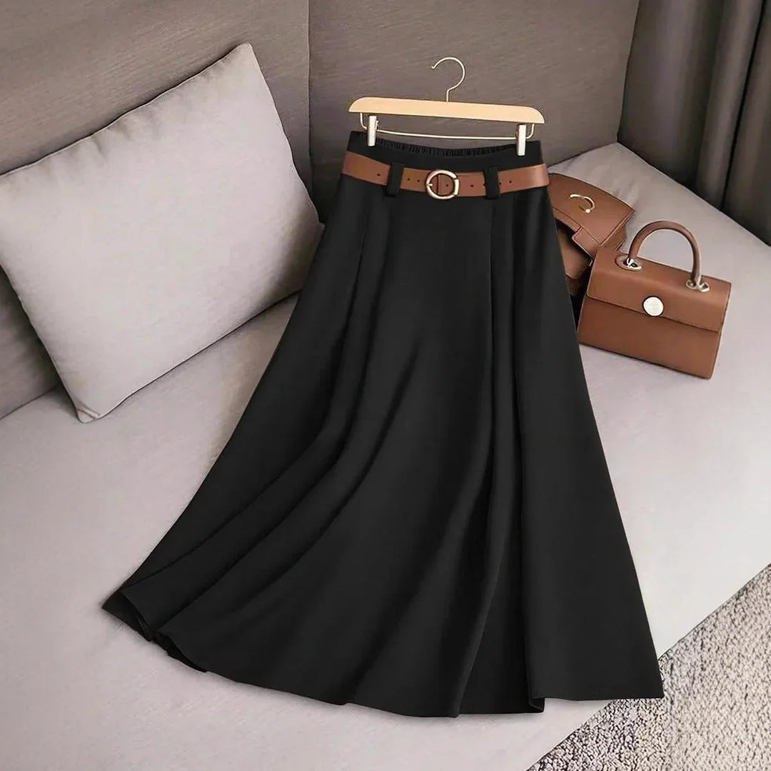 Black pleated midi skirt with brown belt on a hanger on beige couch with brown handbag