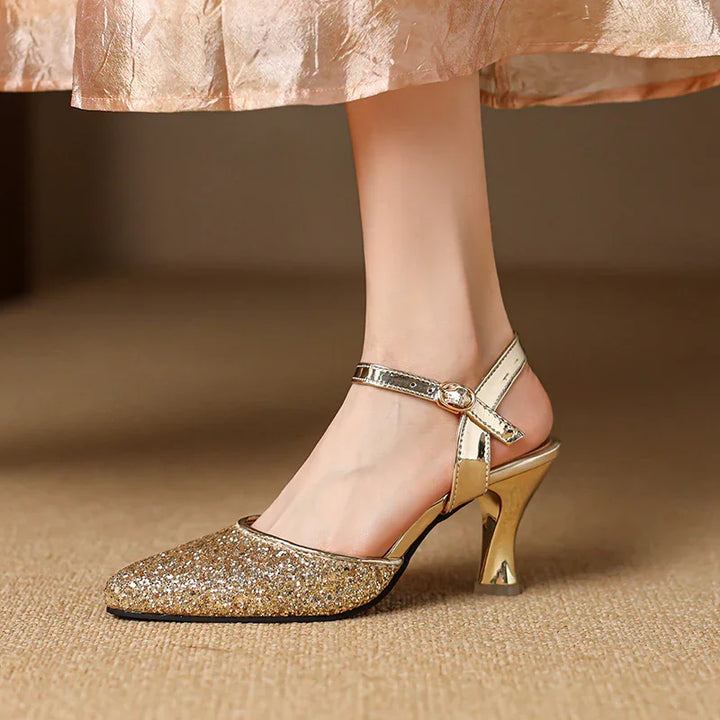 Women's gold glitter pointed toe high heel shoe with ankle strap on carpet