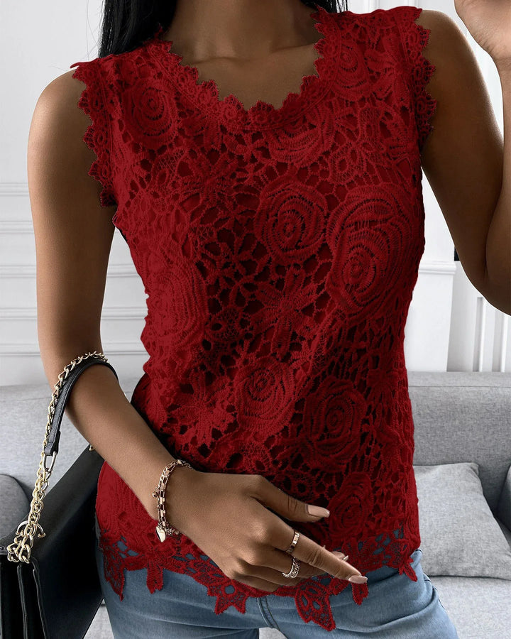 Woman wearing sleeveless red lace top with floral patterns and blue jeans indoors
