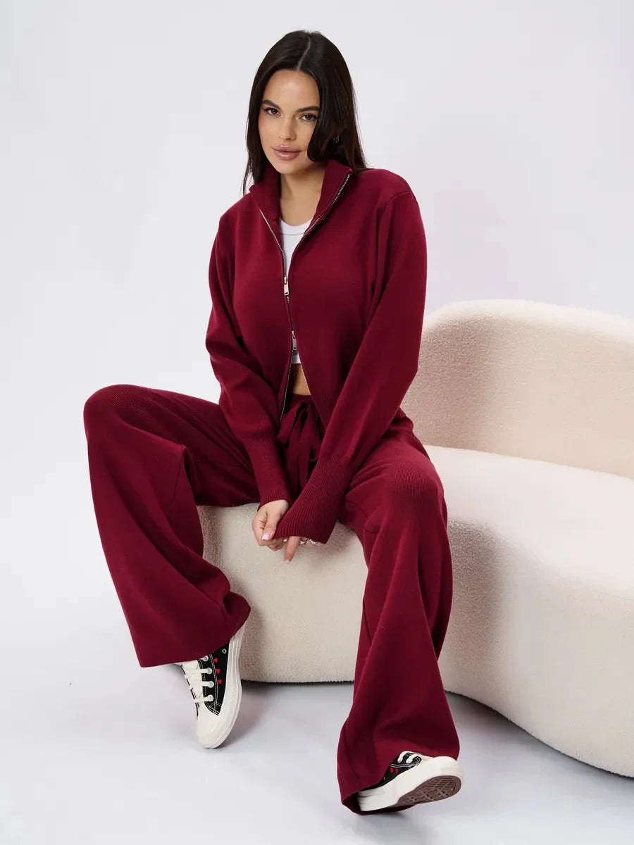 Woman wearing burgundy knit zip-up jacket and wide-leg pants sitting on cream curved sofa