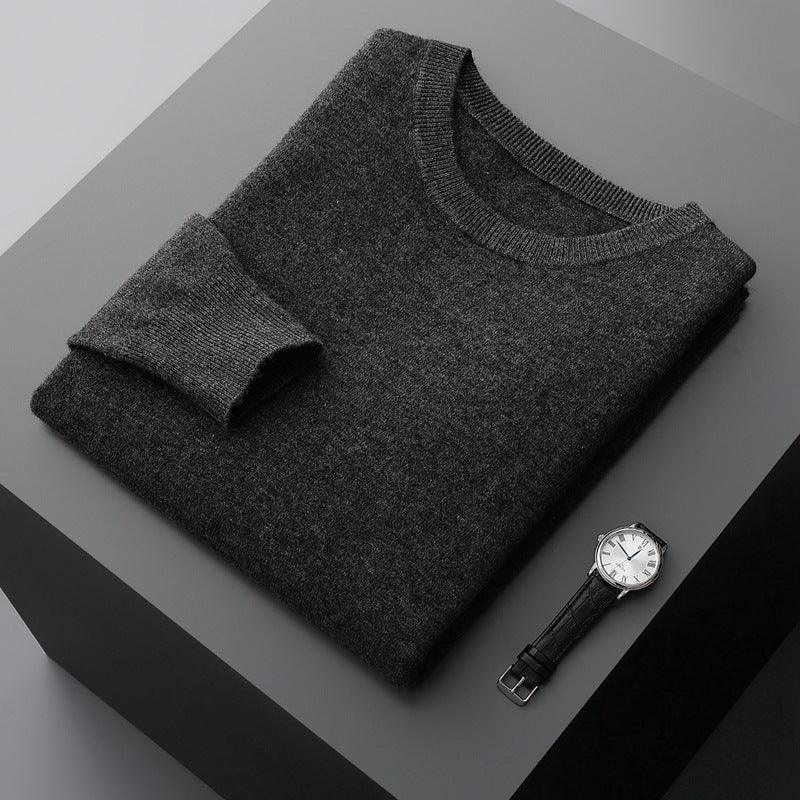 Folded dark gray wool sweater with black leather strap wristwatch on gray surface