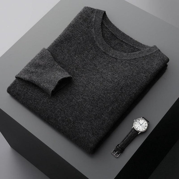 Folded dark gray wool sweater with black leather strap wristwatch on gray surface