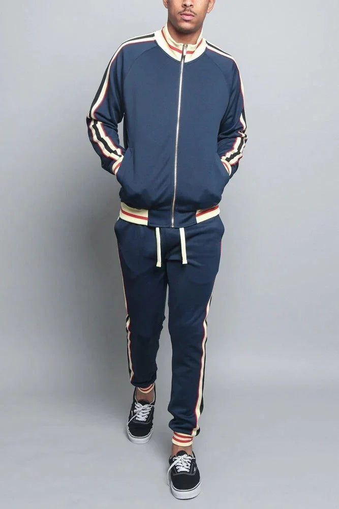 Man wearing navy blue tracksuit with red and white stripes, black sneakers, studio background