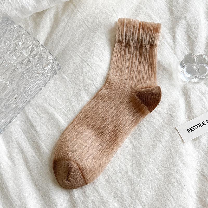 Beige ribbed sock with brown toe and heel on white fabric background, styled with clear glass decor