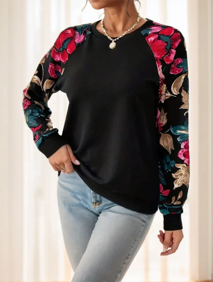 Woman wearing black sweatshirt with colorful floral printed sleeves and light blue jeans