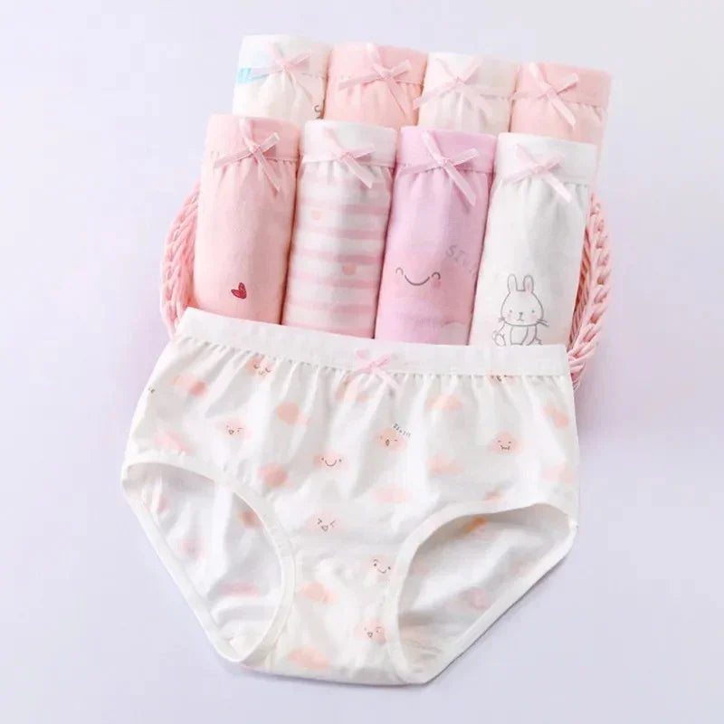 Set of pastel pink and white girls' underwear with cute prints and bows, arranged in a pink basket