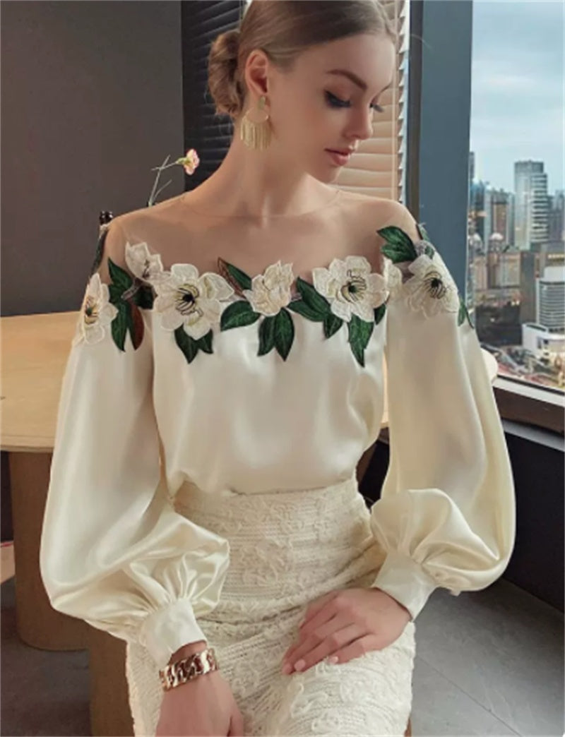 Woman wearing elegant off-shoulder white blouse with floral embroidery and lace skirt in modern setting