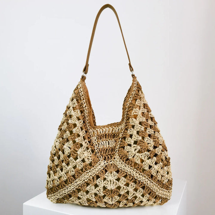 Handwoven brown and beige crochet tote bag with leather strap on white pedestal