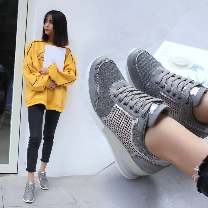 Woman in yellow sweatshirt and black jeans wearing gray casual sneakers against white wall