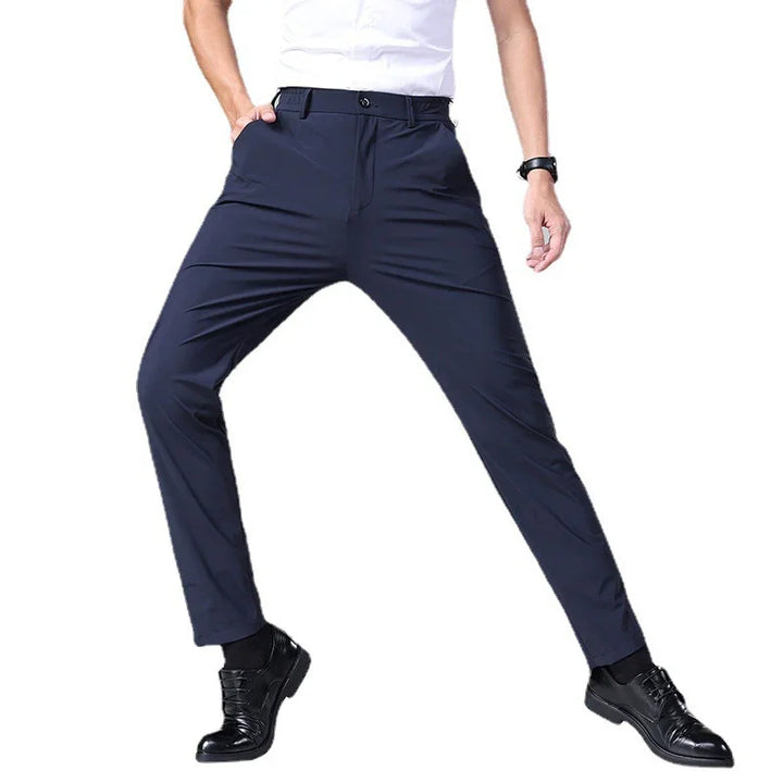 Man wearing navy blue slim-fit pants and black dress shoes against white background
