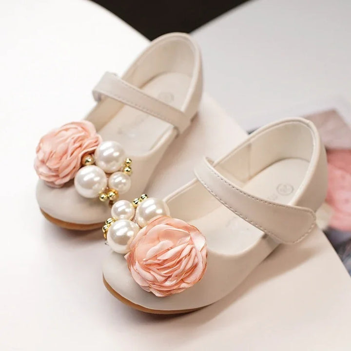 Elegant beige toddler shoes with peach fabric flowers and pearl bead embellishments on white surface