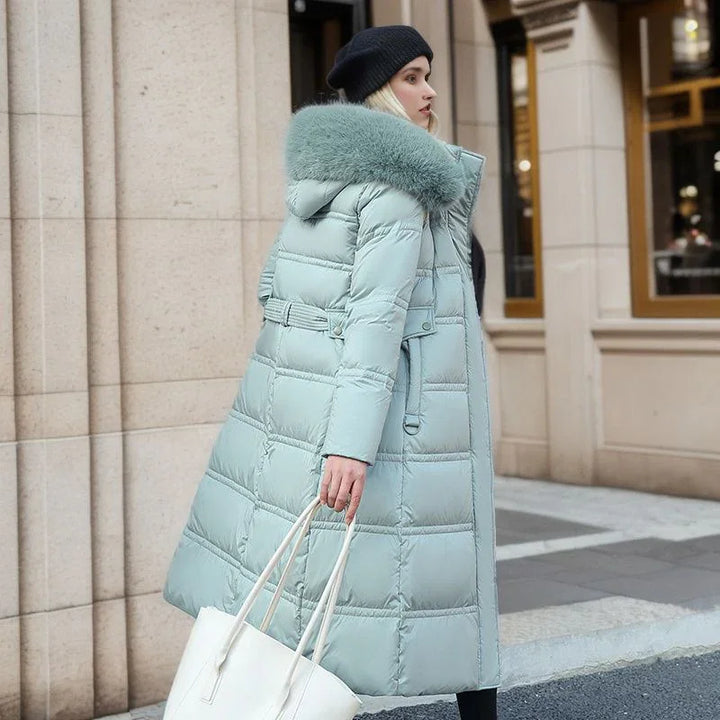 Woman wearing a long light blue puffer coat with fur collar and black beanie, carrying white tote bag outdoors
