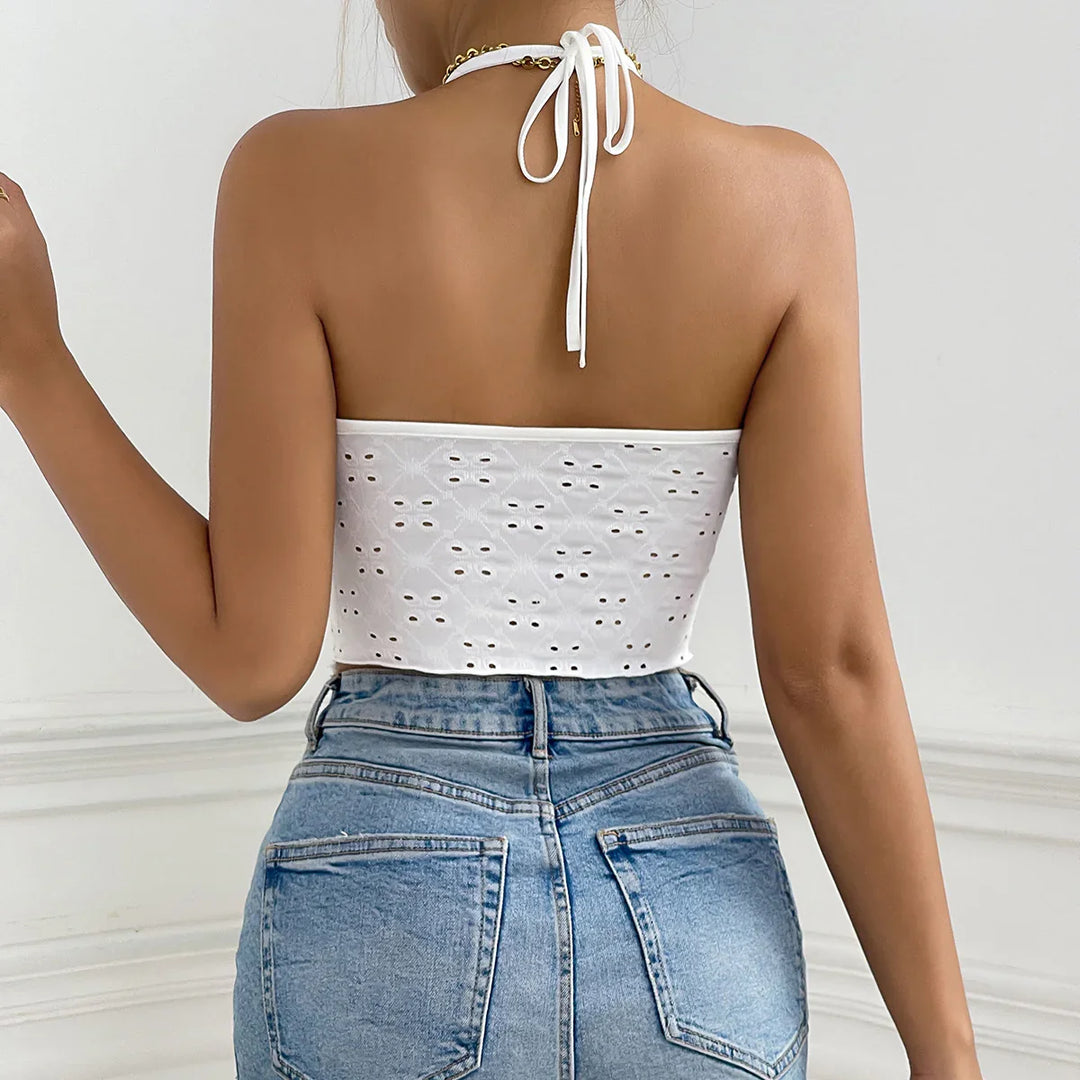 Back view of woman wearing white eyelet halter crop top and high-waisted blue denim jeans