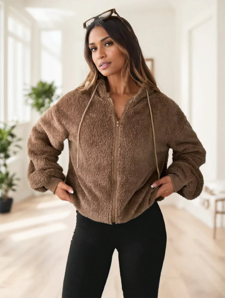 Woman wearing brown zip-up sherpa fleece jacket and black pants in bright indoor setting