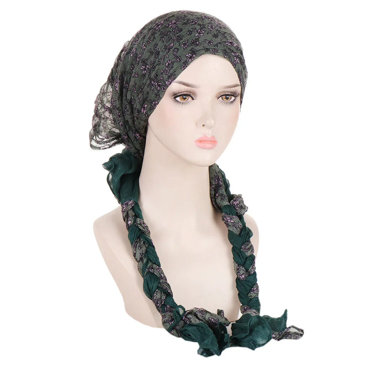 Mannequin wearing a green floral patterned headscarf with braided ends on a white background