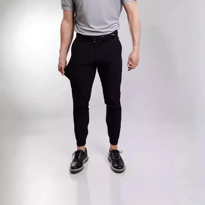 Man wearing black tailored jogger pants and black leather shoes against plain background
