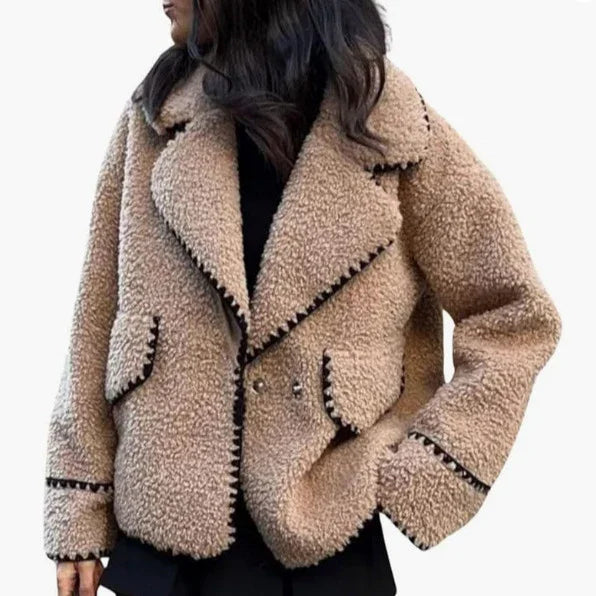 Beige sherpa jacket with black trim worn by woman with dark hair, featuring large collar and pockets
