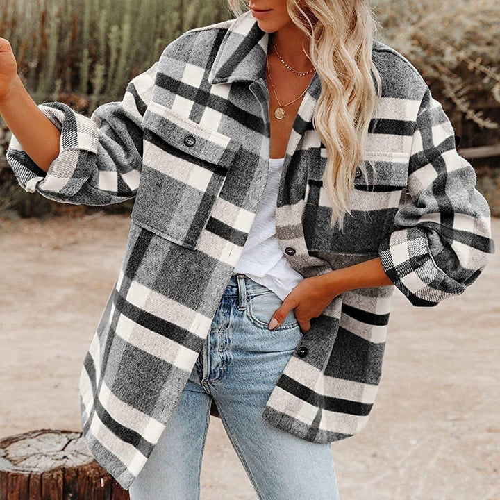 Woman wearing gray and white plaid shacket over white top with jeans in outdoor setting