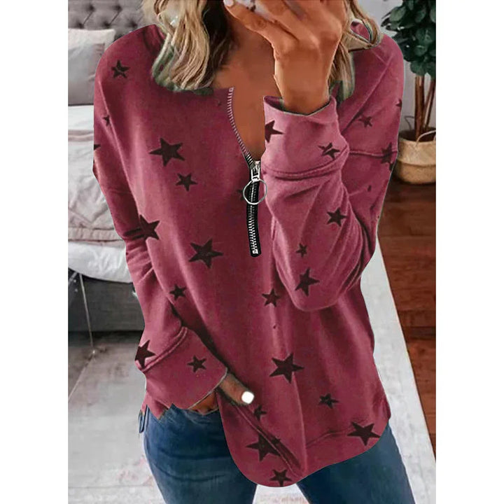 Woman wearing a mauve star-print long sleeve top with front zipper in a cozy living room