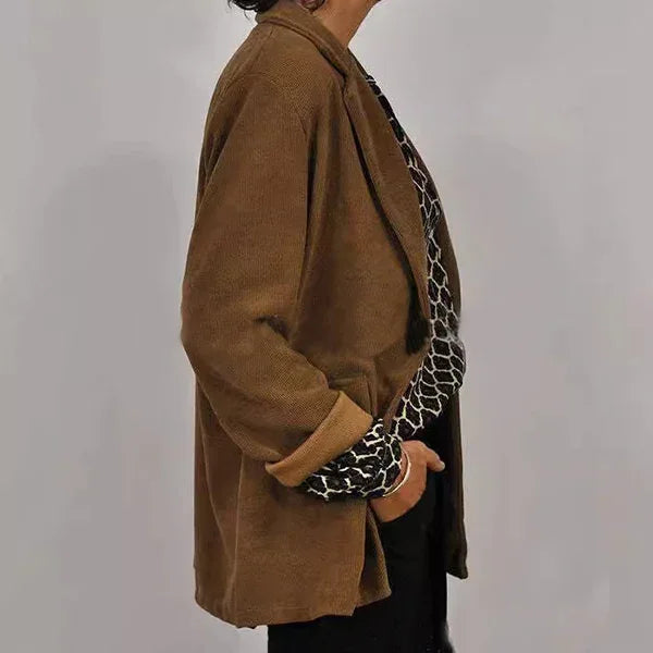 Woman wearing brown corduroy blazer and black-and-white patterned blouse against gray background