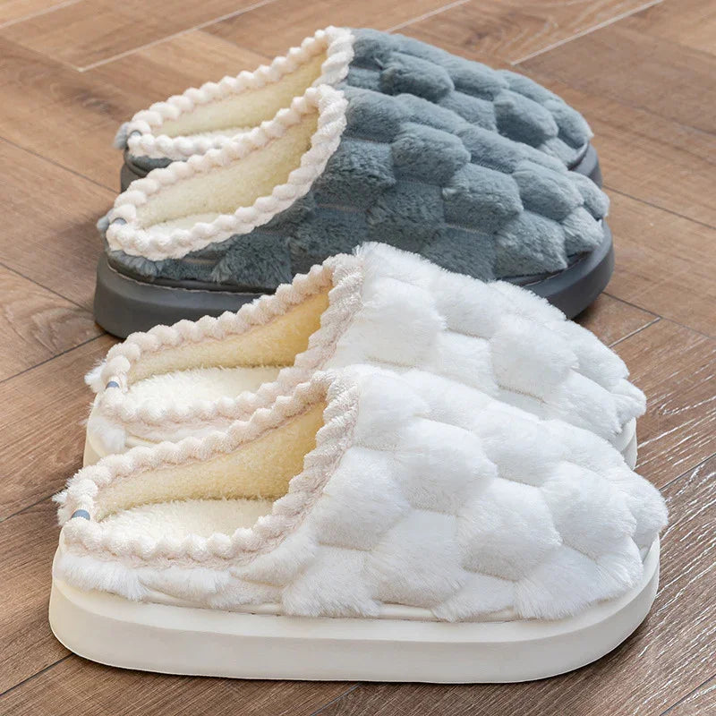 Two pairs of cozy textured slippers with plush lining on wooden floor, one white and one gray