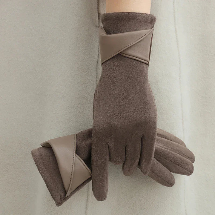 Brown soft fabric gloves with beige leather band detail worn and held against beige coat background