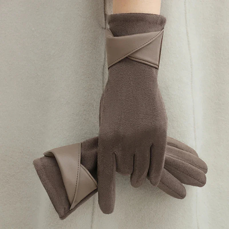 Brown suede gloves with beige leather trim worn on hands against a cream fabric background