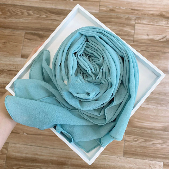 Hand holding a white tray with a neatly rolled pastel blue fabric on wooden floor background