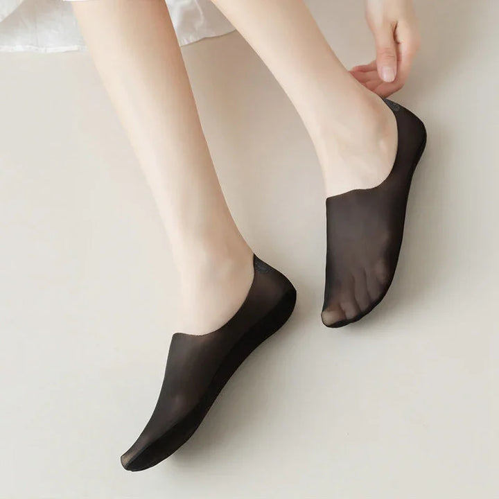 Feet wearing sheer black no-show socks on a light floor surface