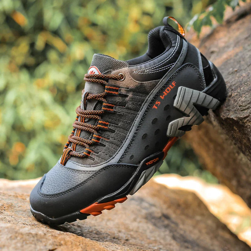 TS Wolf black and orange outdoor hiking shoe on rocky terrain with rugged sole and breathable mesh