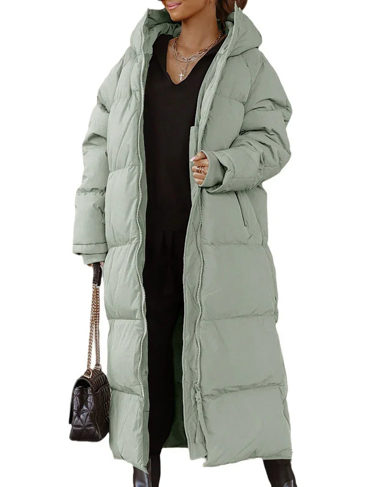 Woman wearing long light green puffer winter coat with hood and black outfit holding black handbag