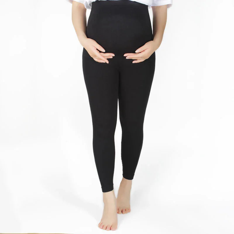 Pregnant woman wearing black maternity leggings standing barefoot on white background