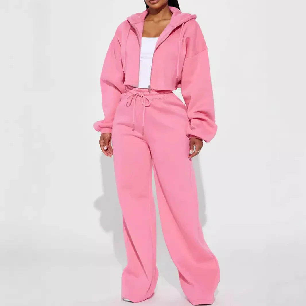 Woman wearing a pink hooded cropped jacket and matching wide-leg pink sweatpants with a white top