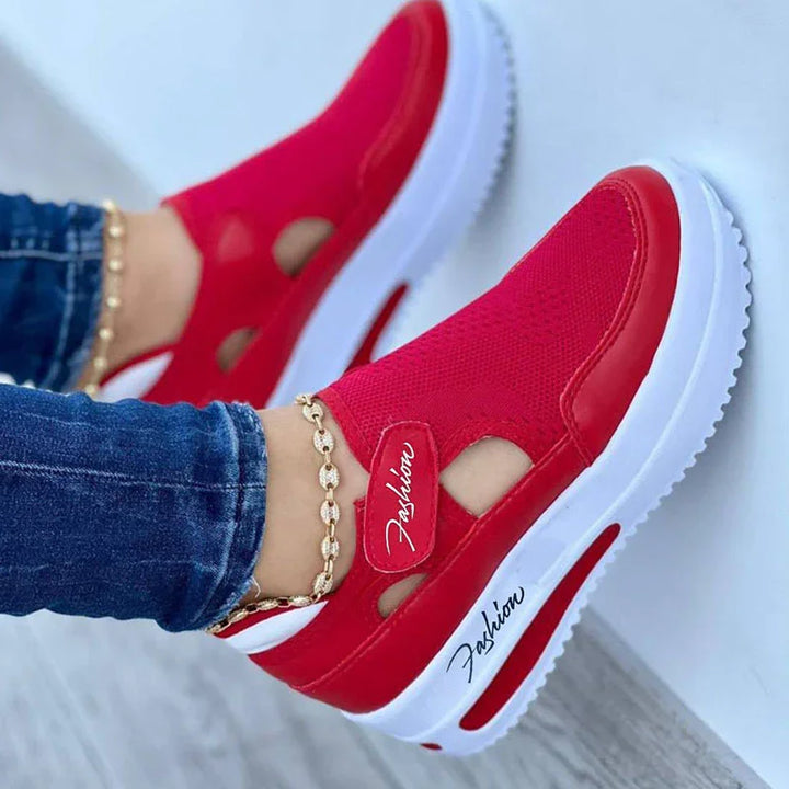 Red slip-on platform sneakers with white soles and cutout design worn with blue jeans and gold anklet