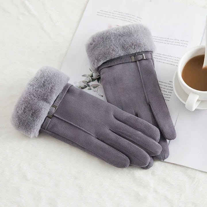 Pair of gray suede winter gloves with plush fur cuffs on white background next to coffee cup