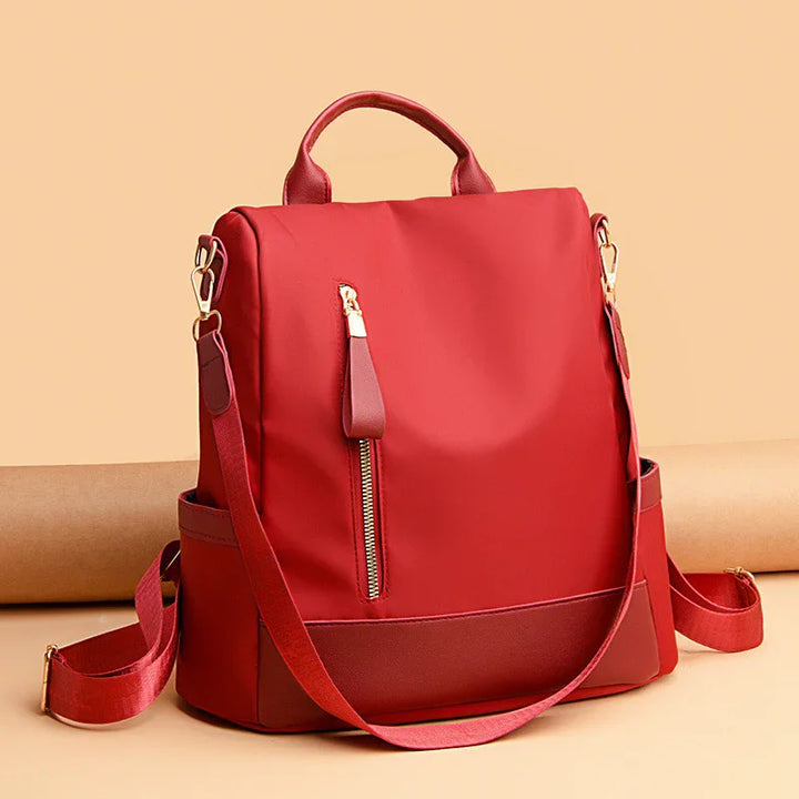 Red nylon backpack with leather accents, front zipper pocket, and adjustable shoulder straps
