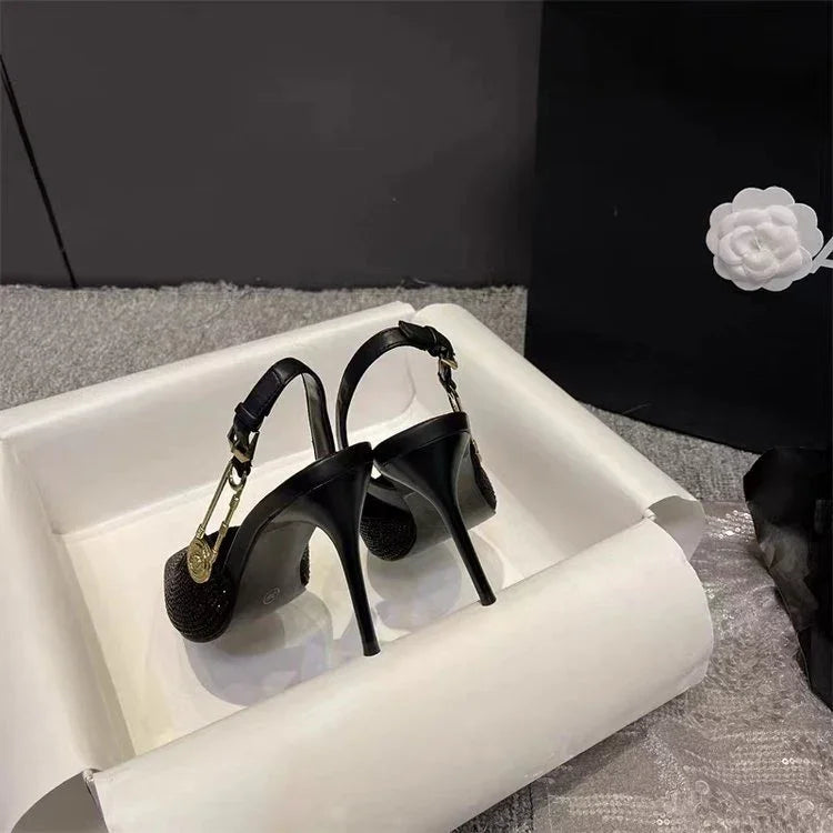 black high-heeled slingback shoes with gold buckle detail in a white box