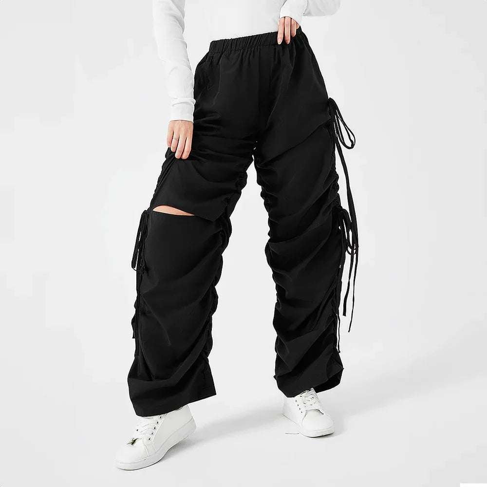 Modern black cargo pants with drawstrings and a knee cutout, styled with white sneakers